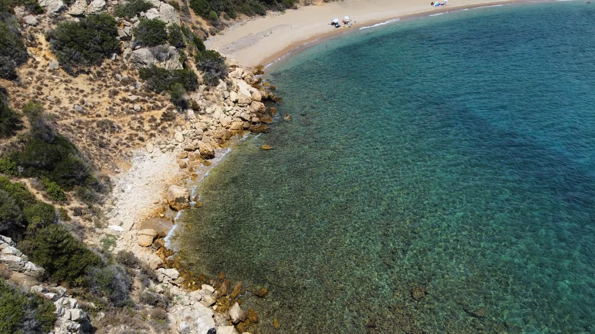 Aerial shot of a serene beach cove with clear turquoise waters and rocky shoreline.